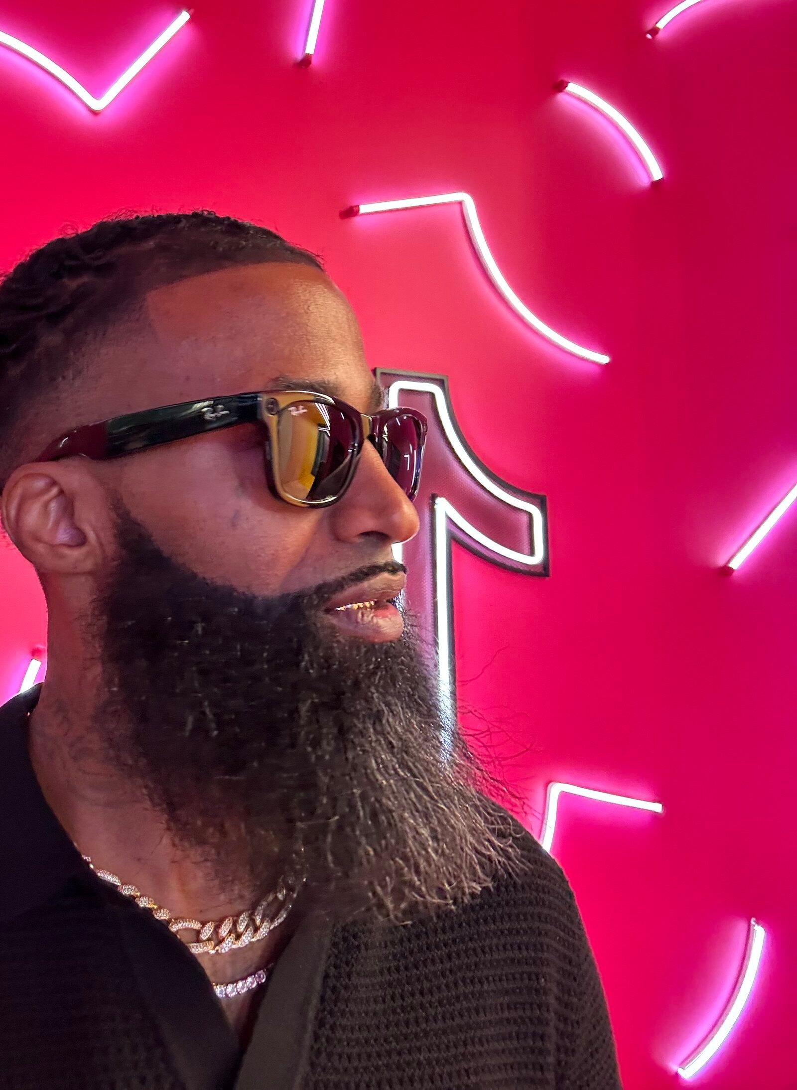 Whoa Nahh in profile against the pink neon wall at a TikTok creator space, sunglasses and layered chains, as photographed